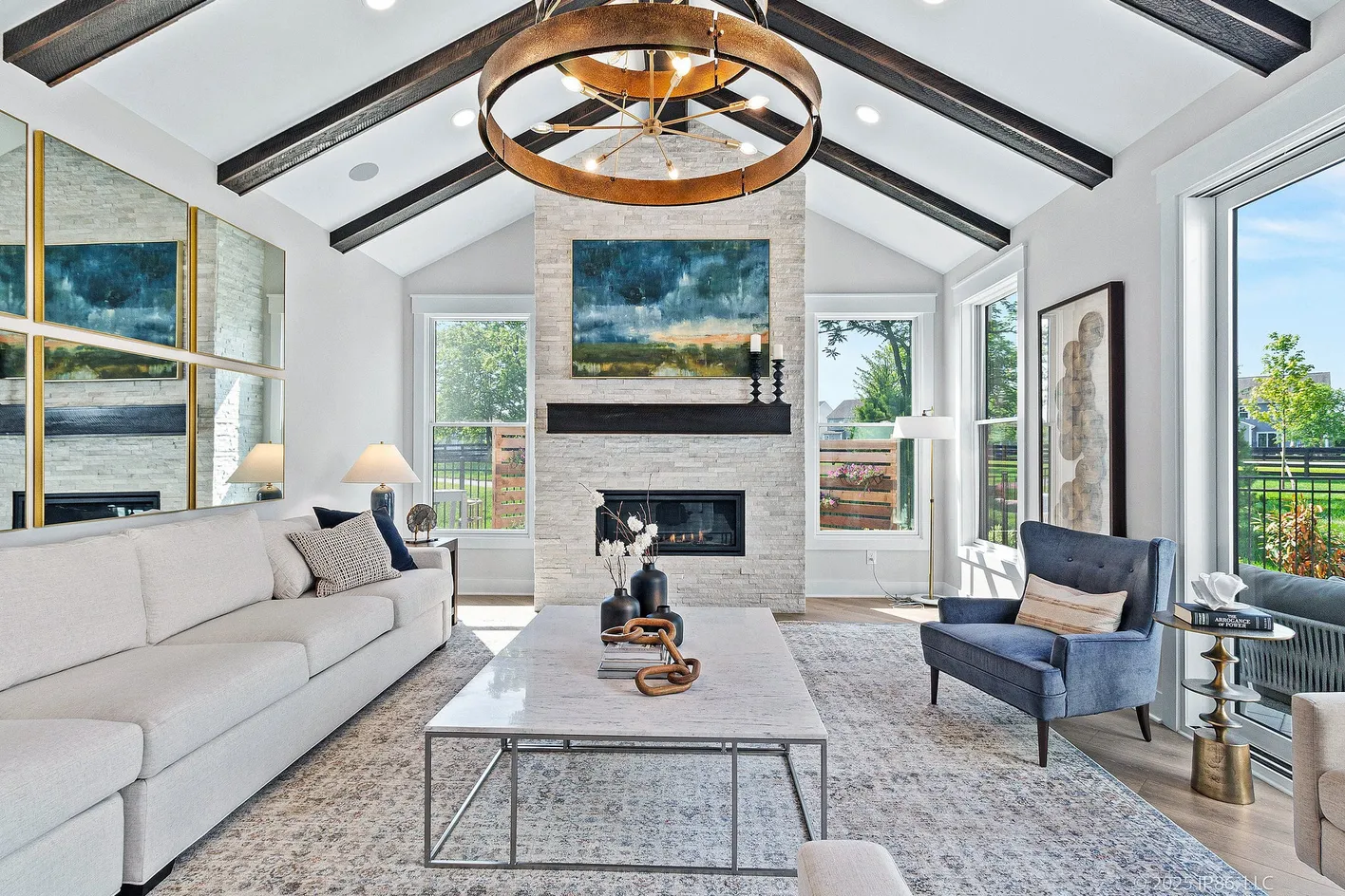 Bright living room with vaulted ceiling, exposed beams, fireplace, large windows, and seating area with sofa and chairs