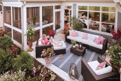 Courtyard patio with wicker sectional seating, pink accent pillows, potted flowers, and a woman relaxing outdoors