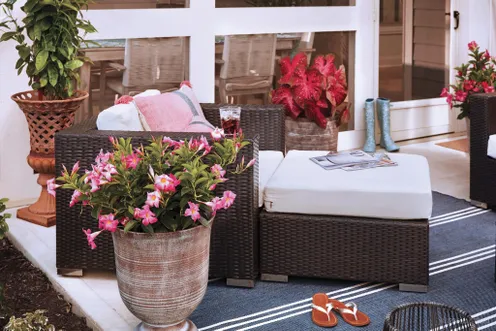 Close-up of patio seating with cushioned ottoman, flowers in planters, and decorative accents